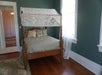 A four post bed with lace hanging over it and several pillow piled at the head of the bed in a teal room with a window on the right.
