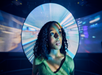 A woman with curly hair stands in front of a large, circular, futuristic screen displaying a motion-blur background.