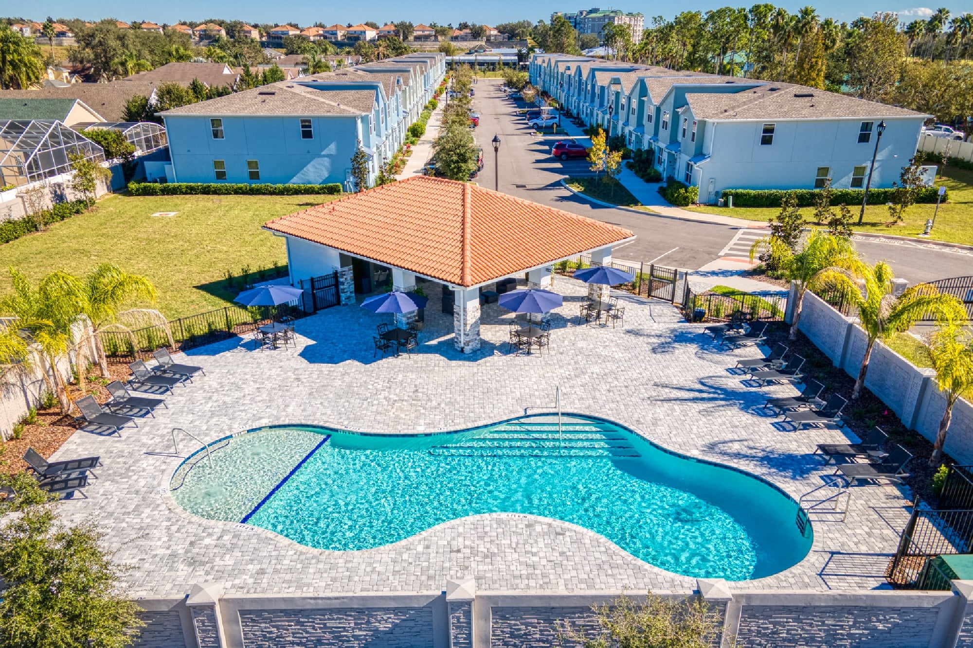 Aerial view of a residential complex featuring a central swimming pool, surrounded by blue buildings and landscaped areas.