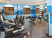 A gym with exercise bikes, ellipticals, weights, exercise balls, benches, and a towel rack, set in a blue-walled room with windows.