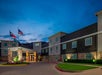 Exterior view of a modern hotel building at dusk with a Four Points sign, two flagpoles, and illuminated entrance.