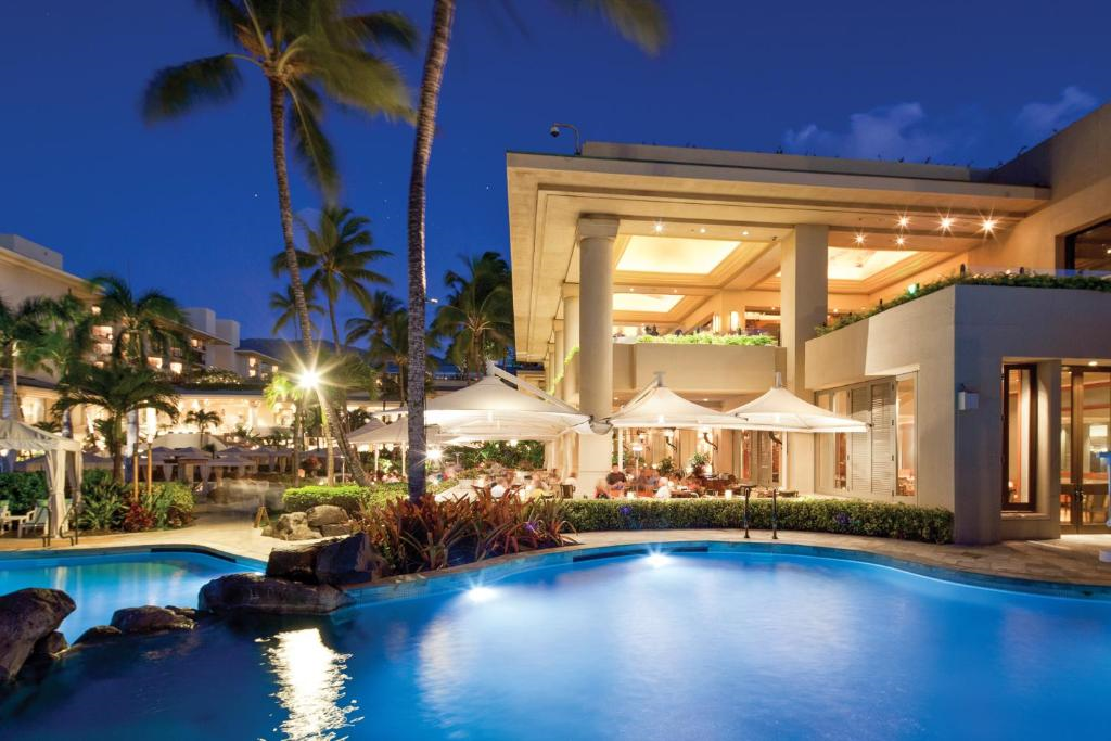 A nighttime view of a resort with illuminated buildings and palm trees surrounding a swimming pool.