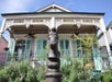 Historic house with ornate trim and turquoise shutters, behind a wrought iron fence with a horse-head hitching post in the foreground.