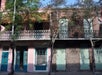 A two-story building with a balcony, featuring pink and brick exteriors, blue and green doors, and trees in front.