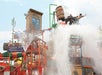 A large bucket tips over, splashing water onto people at a western-themed water park structure with colorful slides and a "Sheriff Office & Jail" sign.