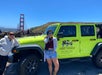 Two women stand next to a bright green San Francisco Jeep Tours vehicle with the Golden Gate Bridge visible in the background on a sunny day.