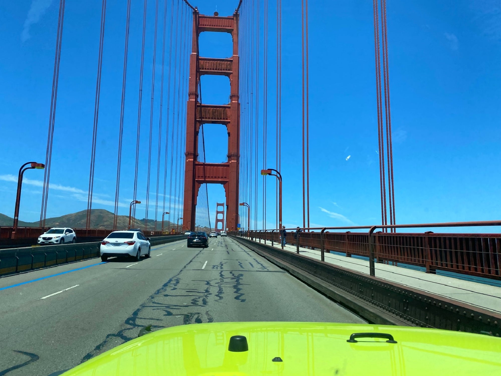 View from a vehicle driving across the Golden Gate Bridge in San Francisco, with cars on the road and clear blue sky above.