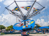 A blue amusement park ride with eagle designs spins with people inside under a partly cloudy sky.