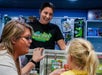 A woman and a child stand at a glass counter with toys behind it, while a staff member in an "Abin Fever Play Centre" shirt smiles at them.