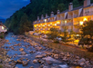 Night view of a lit-up riverside Gatlinburg River Inn with balconies, overlooking a rocky stream surrounded by trees.