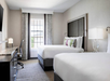 Two queen beds, work desk and a flat-screen TV inside a guest room.
