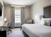 One king bed, arm chair, work desk and a flat-screen TV inside a guest room.