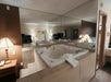 A hotel room with a large jacuzzi tub, mirrored wall, towels, lamps, and a bed visible in the background.