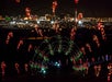 A night view of a city skyline in the background. In the foreground, illuminated arches adorned with red and green lights shaped like candy canes create a tunnel effect.