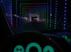 View from inside a car showing a tunnel decorated with colorful LED lights forming square patterns. Dashboard and steering wheel are visible in the foreground.