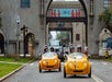 Two sets of tourists wearing helmets and driving yellow GoCars in San Diego with cars on the road behind them on the GoCar Downtown and Balboa Park Tour.