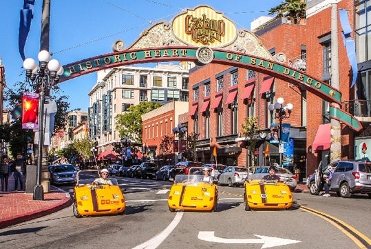 Three tourist in bright yellow GoCars parked under the iconic sign at the entrance to the Gaslamp Quarter on a sunny day in San Diego.