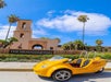 A bright yellow GoCar parked in front of the well landscaped sign for The Headquarters At Seaport District on a sunny day.