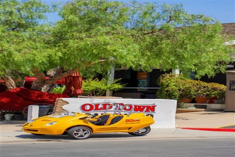 A bright yellow GoCar parked in front of a white and red sign saying "OLD TOWN" on a sunny day in San Diego.