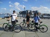 Three tourists holding a bike from Boston Bike Rental and Boston skyscraper on the background with Go City - Boston All-Inclusive Pass.