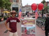A person wearing a harvard hat and a purple shirt with "HAHVAH" printed on it standing beside a Harvard poster during The Harvard Tour with Go City - Boston All-Inclusive Pass.