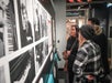 A group of people standing indoors, looking at a poster on a wall that appears to be related to an art exhibition at the Rature Gallery, featuring the artist Haiyg Eteclerc at the American Writers Museum in Chicago.