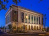 A large, historic stone building with columns houses The Mob Museum; banners display its name. The building is lit at dusk, with trees and a street in the foreground.
