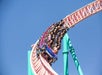 A full roller coaster car of people descends a steep, curved track under a clear blue sky.