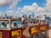 Red double decker bus by Big Bus Tour with several people aboard on it and a beautiful Miami skyscraper on the background with Go Miami All-Inclusive Pass.