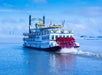 A paddlewheeler boat called the Creole Queen cruising on the water on a cloudy sky.