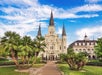 Jackson Square in New Orleans, featuring a clock tower and an outdoor scene includes a cloudy sky, grass, palm trees, and a building with a steeple, showcasing a blend of medieval architecture and a place of worship.