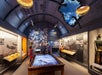Groups of people at an exhibit called "TURNING THE TIDE" at The National WWII Museum on a room with designed interior and ceiling. 