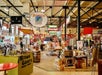 The stores at the Southern Food and Beverage Museum with various signs displayed on the walls and ceilings. The signs include "BLUEBIRD CAFÉ," "AMERICAN," "TOREATIVER," "Browning's," "AL COPELAND," "KITCHEN GADGETS." 