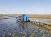 An airboat on standby on the water by the bridge owned by Gator Park Airboat Tour.