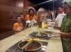Three kids and a woman having a fun time learning how to make chocolates from two chefs at the chocolate factory.