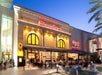 Exterior view of The Cheesecake Factory with several people seated outside.