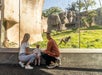 A family with a child watches a monkey through a glass enclosure at a zoo.