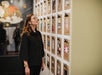 Person looking at a wall display of clipboards with various items attached in an art gallery setting.