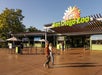 Entrance of San Diego Zoo with two people walking, green ticket booths, and zoo sign featuring a stylized sun and lion.