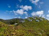 A dome-shaped green roof with circular skylights is covered in vegetation, set against a blue sky with scattered clouds and a distant hill.