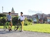 Two people wearing helmets stand with bicycles on a path in front of the Ghirardelli building and sign on a sunny day.