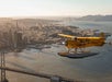 A yellow seaplane flies over San Francisco Bay with the city skyline, Bay Bridge, and Golden Gate Bridge visible in the background.