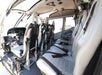 The interior of a small helicopter showing two rows of leather seats, seatbelts, headsets, and the cockpit controls at the front.