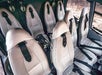 Six cream-colored leather seats with seat belts are arranged in two rows inside a helicopter cabin, with headsets hanging beside each seat.
