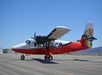 A red and white twin-engine airplane is parked on the tarmac under a clear blue sky, with mountains visible in the background.