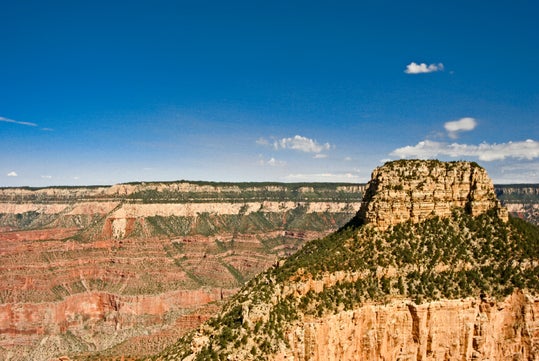 Flat-topped mesa rises above layered red rock cliffs in a canyon landscape under a clear blue sky.