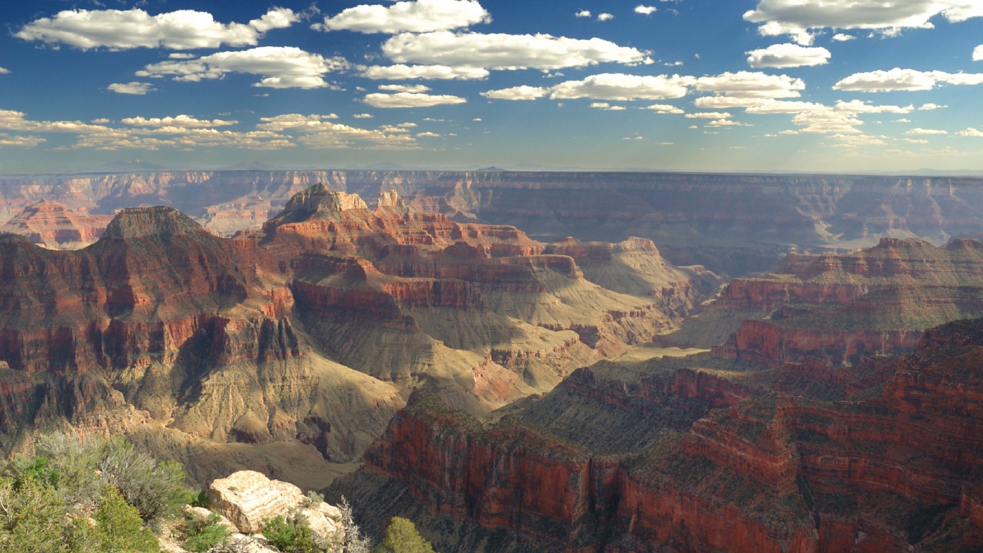 View of the Grand Canyon under a partly cloudy sky, showing layered rock formations and deep, colorful canyon walls.