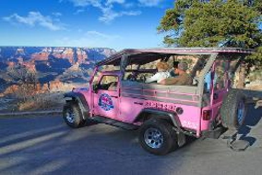A pink tour jeep parked at a scenic viewpoint overlooking the Grand Canyon, with passengers seated inside and clear skies above.
