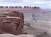 Visitors stand on a glass skywalk overlooking the steep cliffs and canyon walls at the Grand Canyon under a cloudy sky.