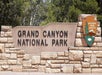 Stone entrance sign for Grand Canyon National Park with the National Park Service emblem, set against a background of trees.